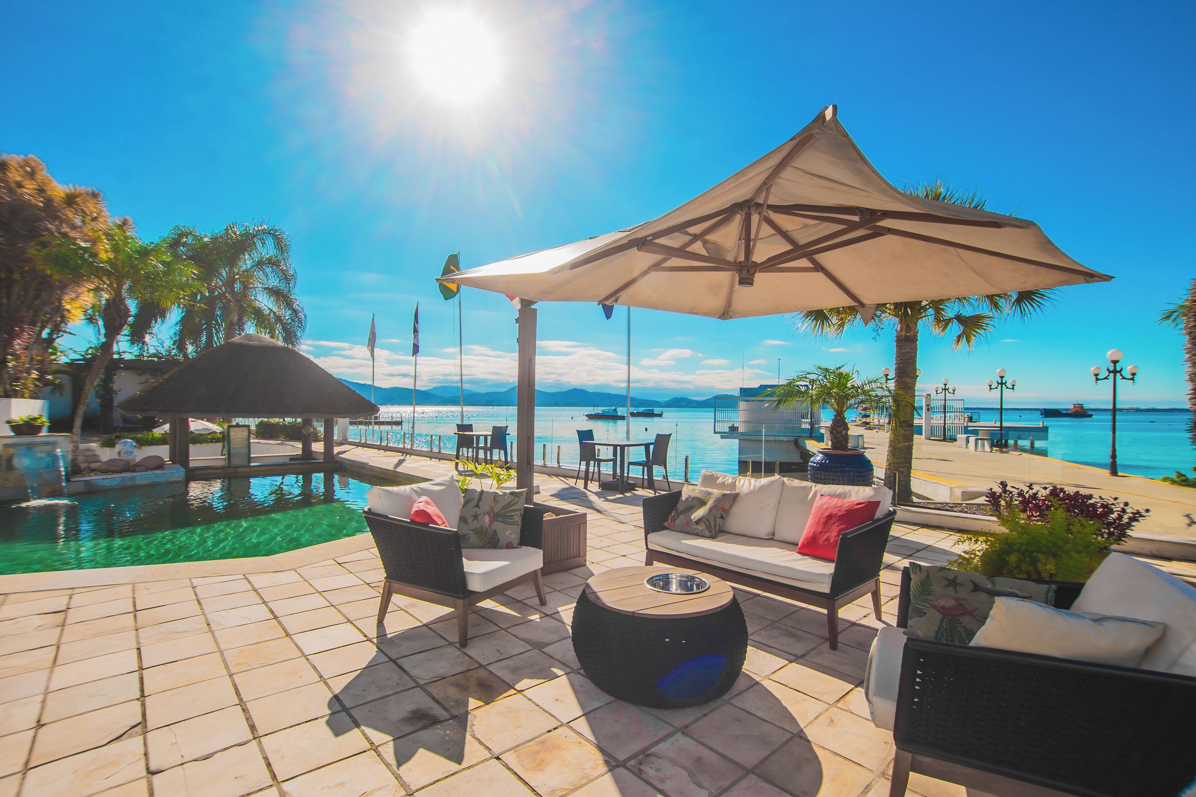 A sunlit outdoor seating area with a pool, lounge chairs, and a large umbrella.