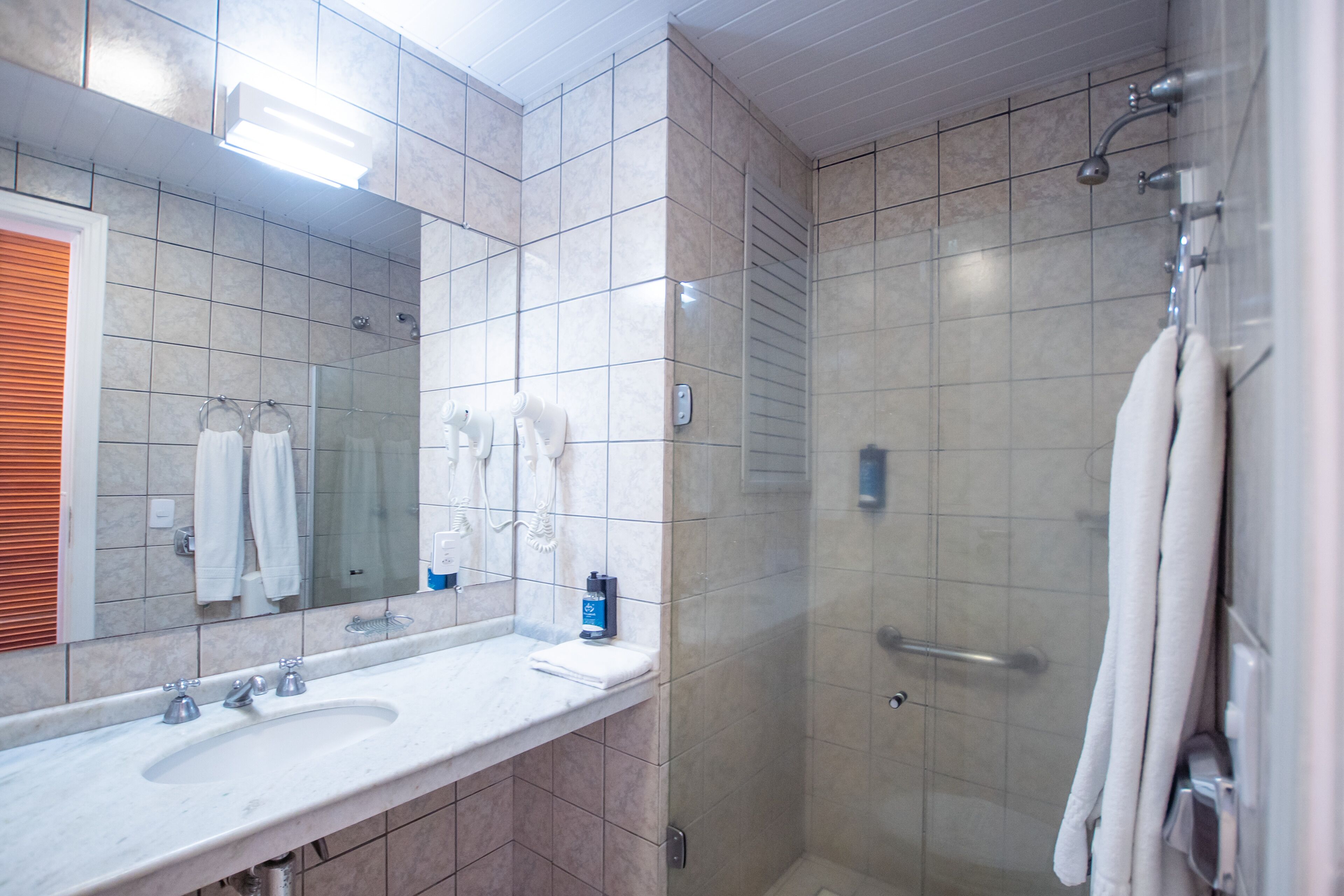 Un baño con un espejo grande, dos lavamanos, una ducha y un perchero para toallas.