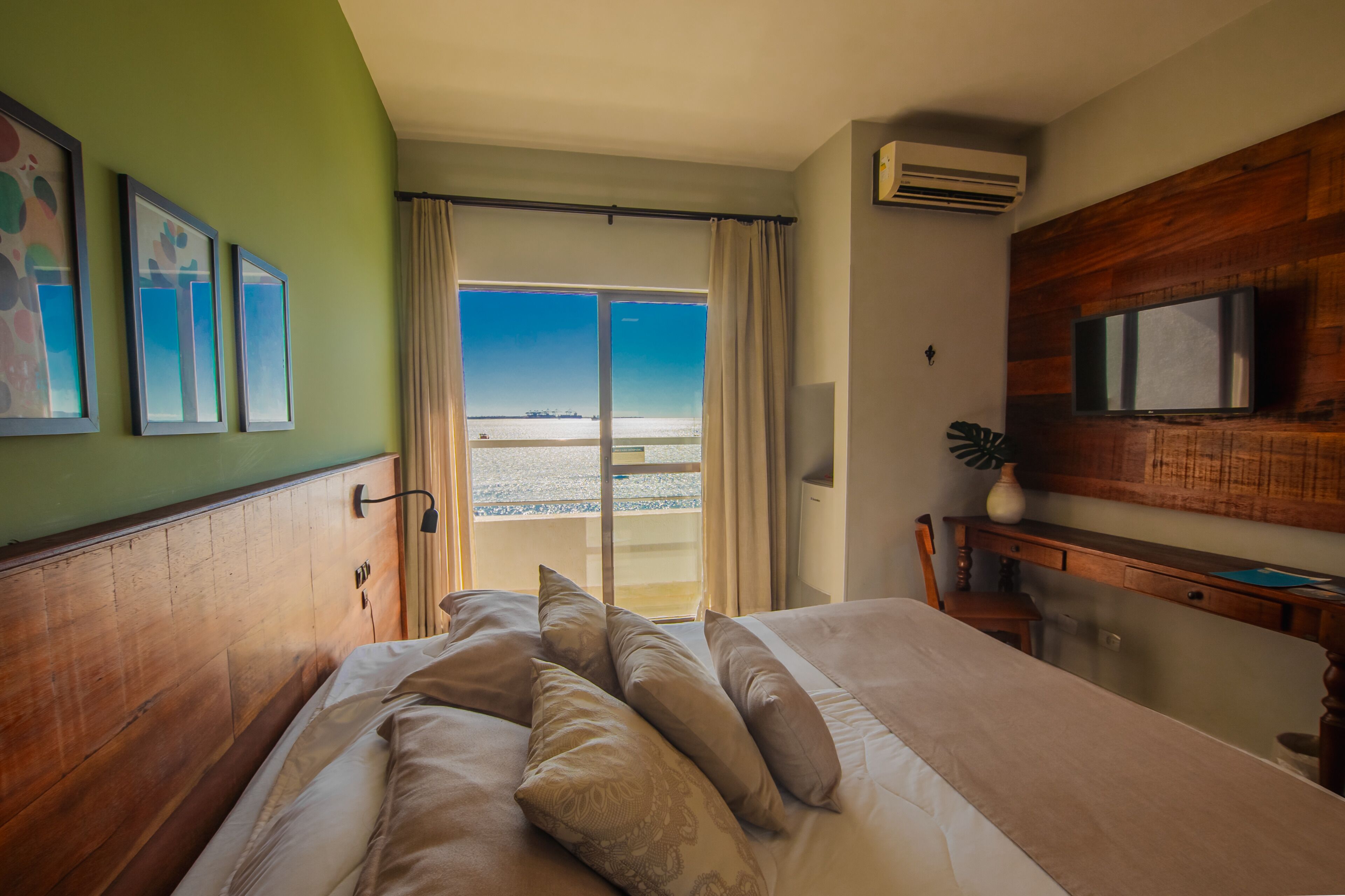 Een hotelkamer met een bed, een bureau, een televisie en uitzicht op het strand.