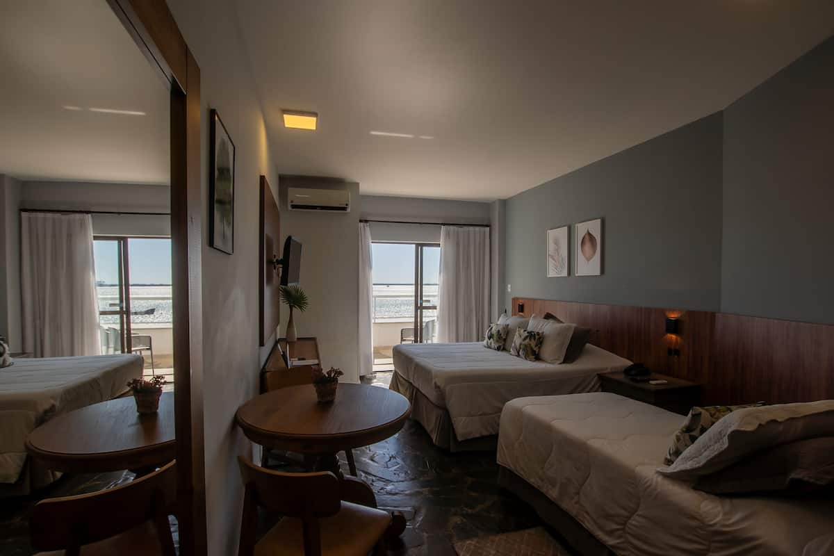 A hotel room with two beds, a dining table, and a view of the beach.