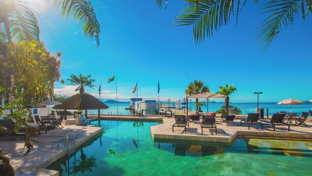 A clear pool with lounge chairs and umbrellas, a view of the ocean, and flags. - Hotel VillaReal Sao Francisco do Sul (São Francisco do Sul)