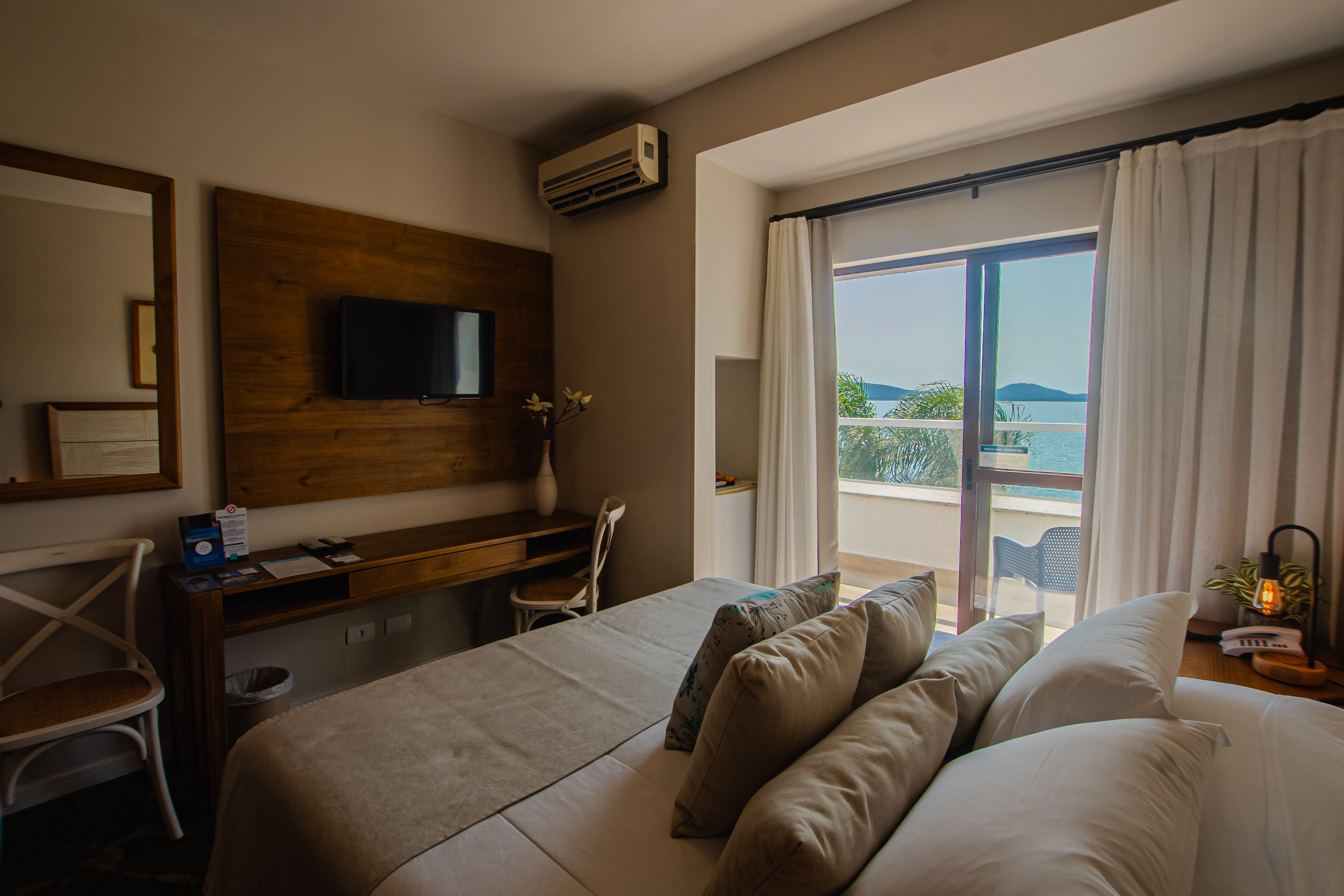 Habitación de hotel con cama, escritorio, silla, televisión y vistas al exterior.