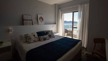 A bedroom with a bed, a nightstand, a chair, and a view of the sea.