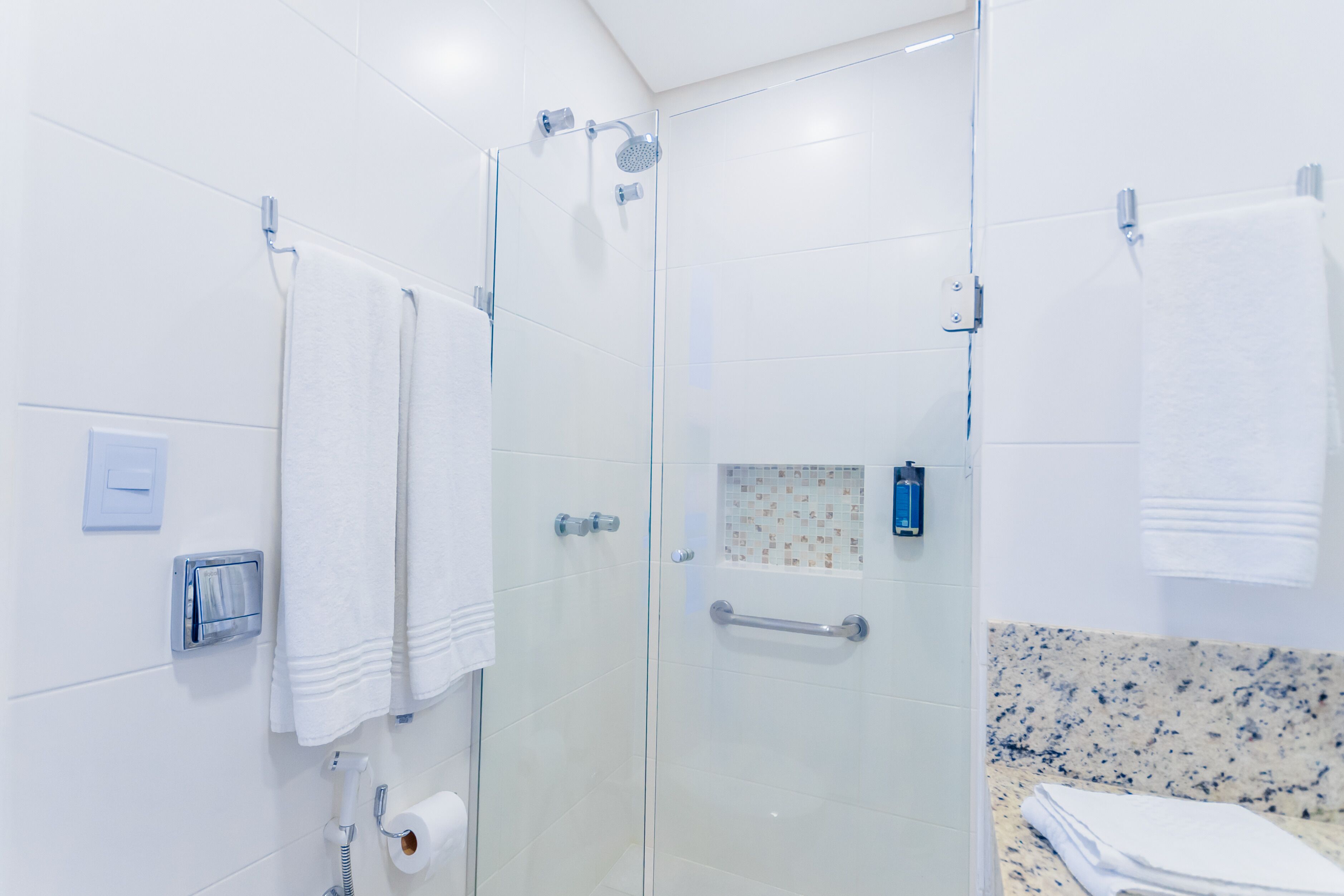 A modern bathroom with a glass-enclosed shower, white tiles, a marble countertop, and a towel rack.