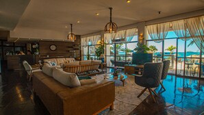 A spacious living area with a large sofa, armchairs, and a coffee table. There is a view of the ocean through large windows. - Hotel VillaReal Sao Francisco do Sul (São Francisco do Sul)