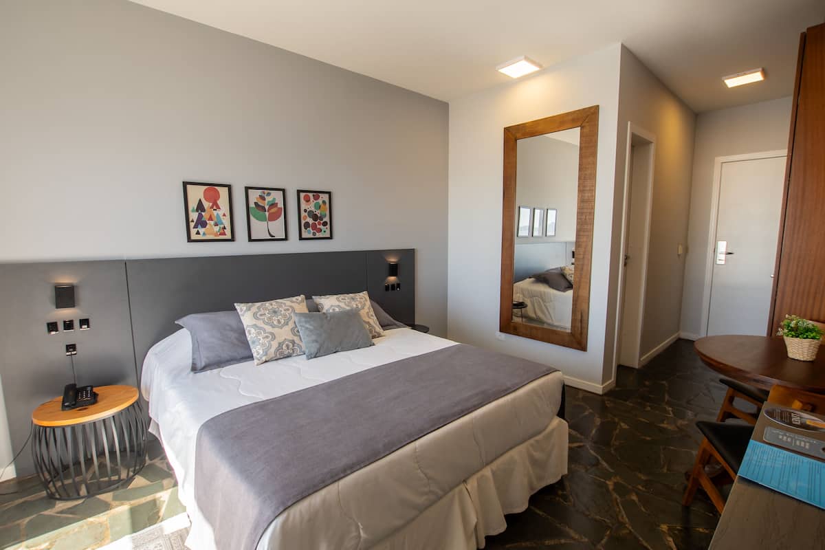 A modern bedroom with a large bed, bedside tables, a mirror, and artwork on the wall.