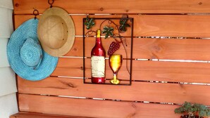A wooden bench with a metal shelf above it, holding a hat, a wine bottle, and a glass.