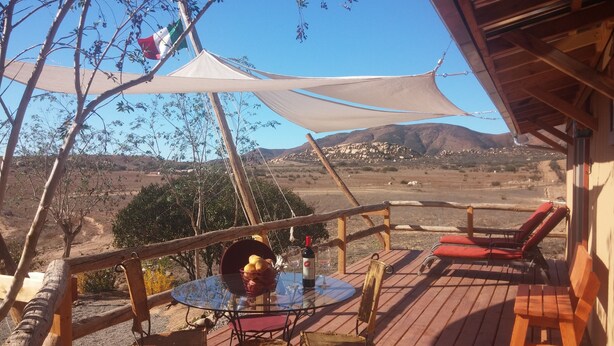 A wooden deck with a glass table, red chairs, and a view of a mountainous landscape.
