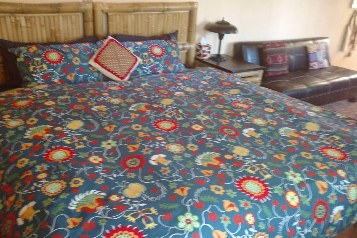 A bed with a floral-patterned bedspread, a wooden headboard, and a nightstand with a lamp.
