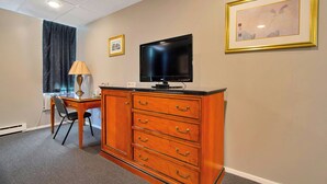 Quarto de hotel com cómoda de madeira, escrivaninha, cadeira, televisão e duas molduras na parede.