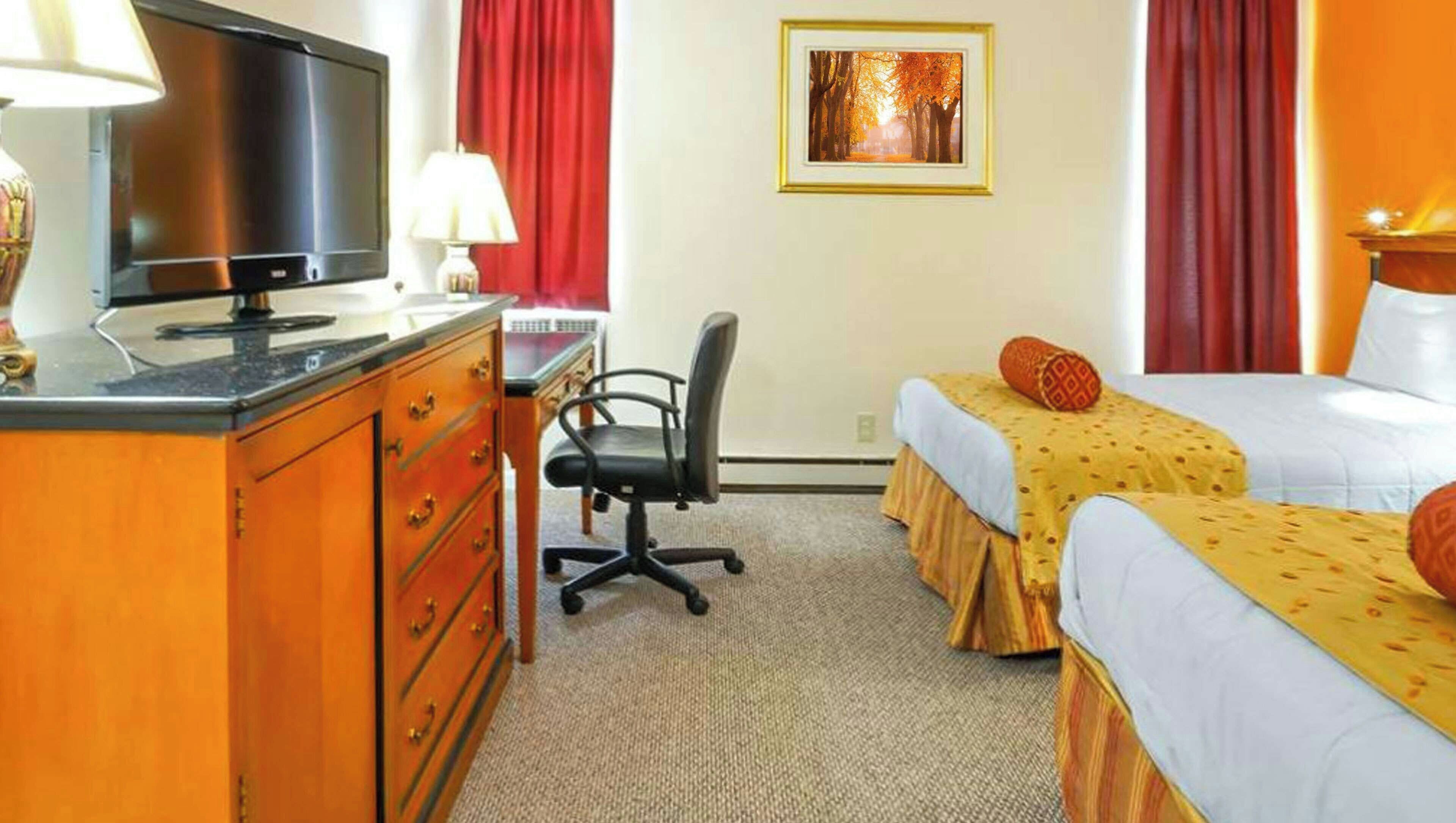 A hotel room with a desk, chair, two beds, a TV, and a framed picture on the wall.