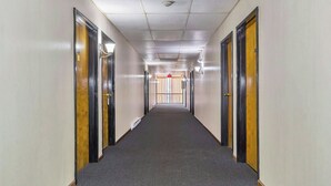 Corredor de hotel com portas em ambos os lados, piso coberto de carpete e um alarme de incêndio no final.