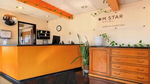 Uma mesa de recepção com um relógio, um espelho e uma placa indicando MSTAR HOTEL NORTH CANTON.