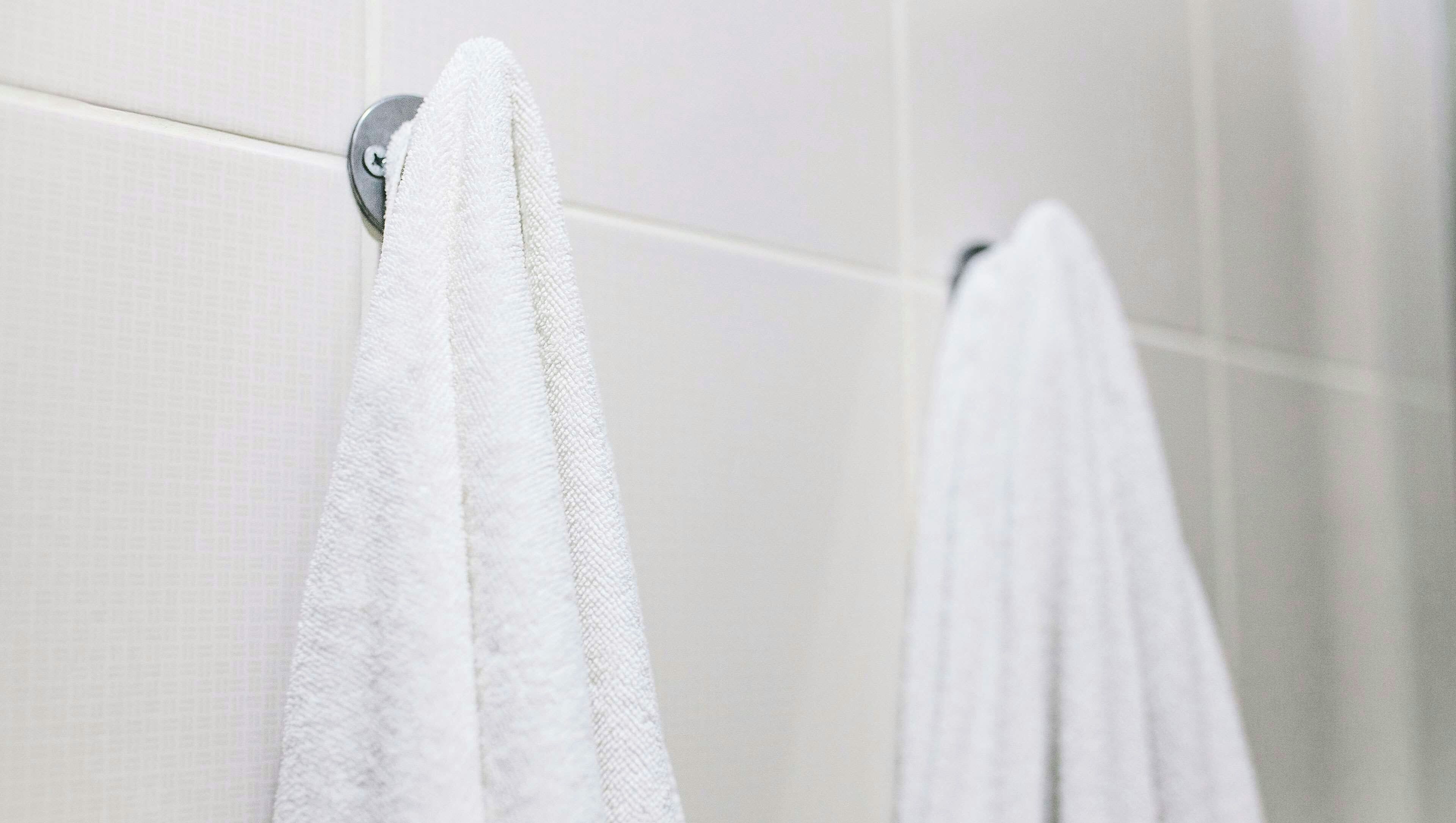 Un baño con paredes de azulejos blancos y dos toallas blancas colgadas en un perchero metálico.