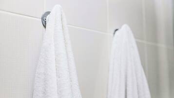 Un baño con paredes de azulejos blancos y dos toallas blancas colgadas en un perchero metálico.