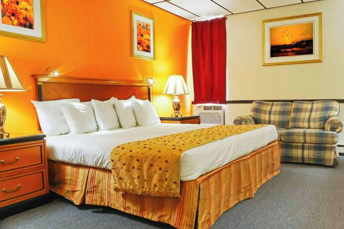 Una habitación de hotel con una cama, una silla, una mesita de noche, una lámpara y un cuadro en la pared.