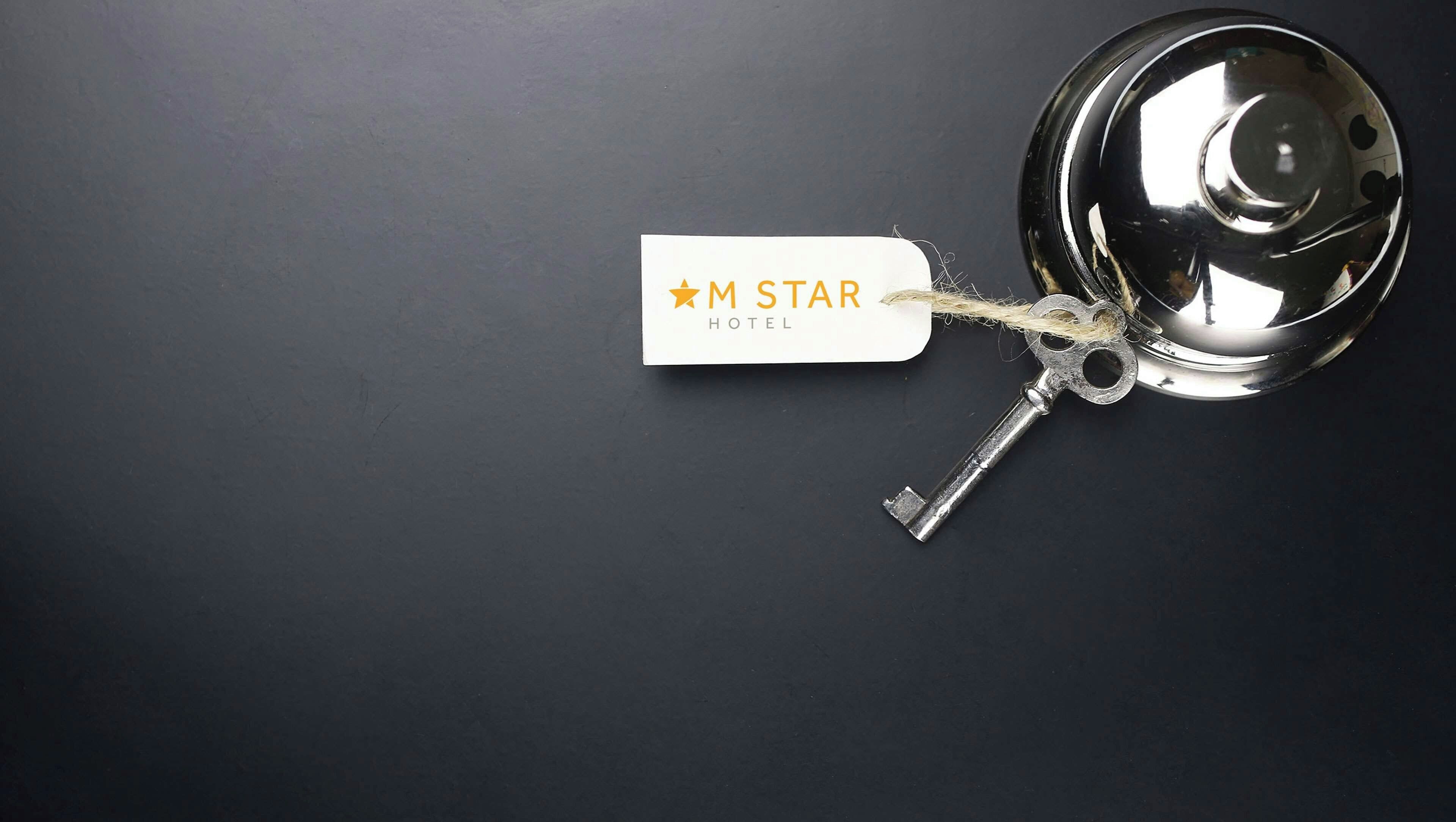 Avain, joka on kiinnitetty hotellin avaimenperään, jossa lukee ”M STAR HOTEL”, ja avain on asetettu tummalle alustalle.