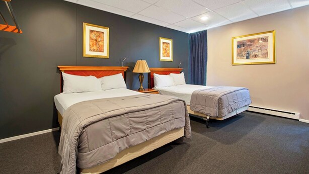 Quarto de hotel com duas camas, uma mesa de cabeceira com abajur e quadros decorativos nas paredes.