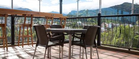An outdoor patio with a table and chairs, a tiled floor, and a view of a mountainous landscape.