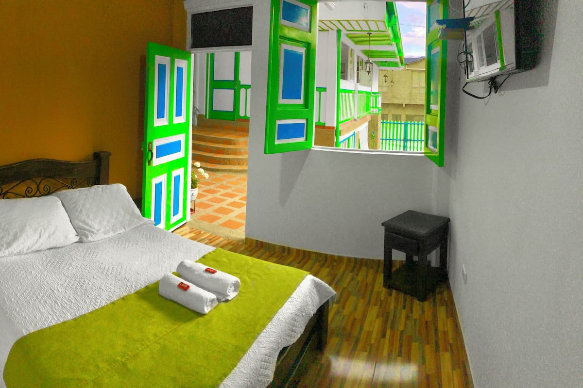 Ein Zimmer mit einem Bett, einem kleinen Tisch und einem Fenster mit grünen Fensterläden.