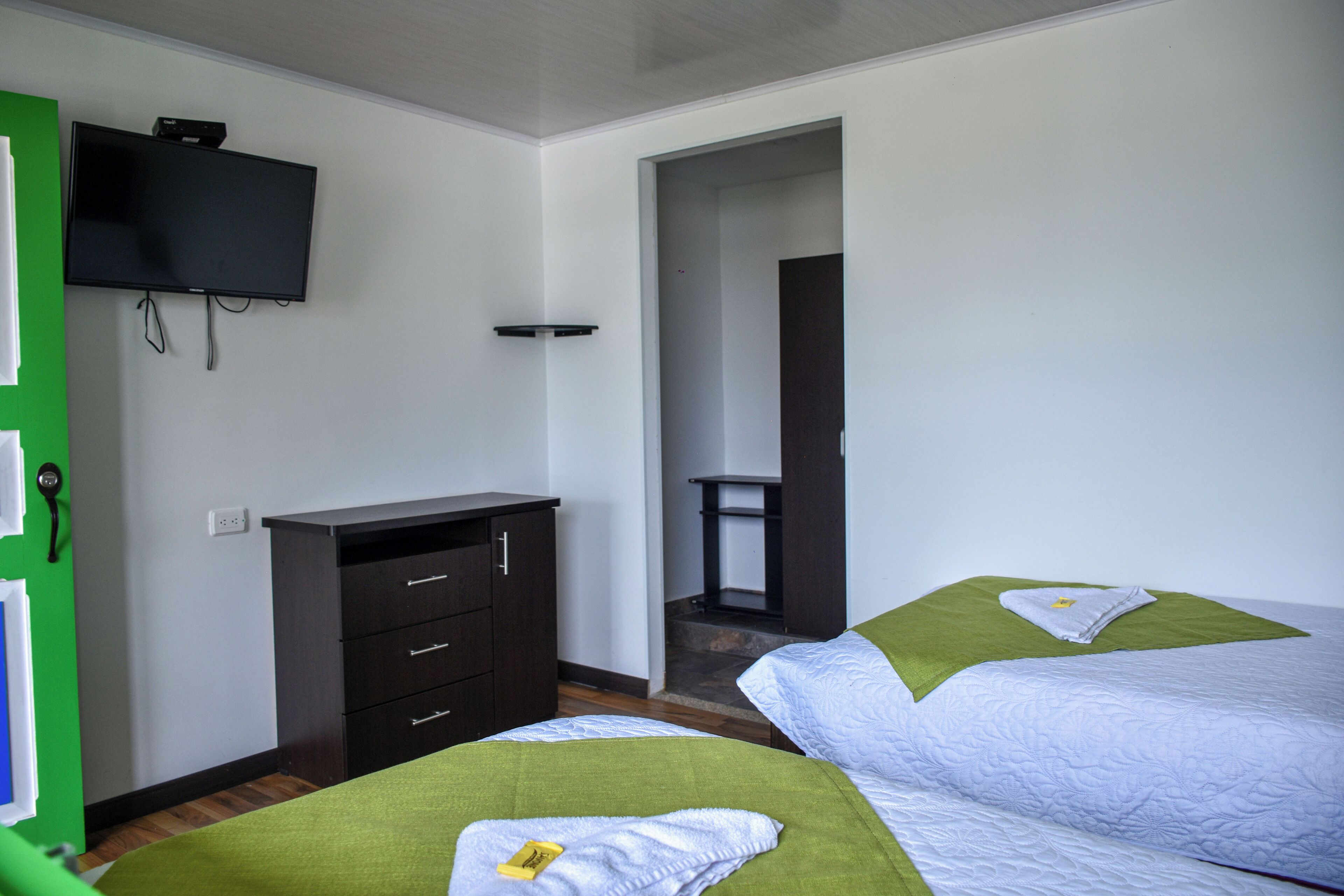 Een hotelkamer met twee bedden, een aan de muur bevestigde televisie, een bureau en een groene deur.