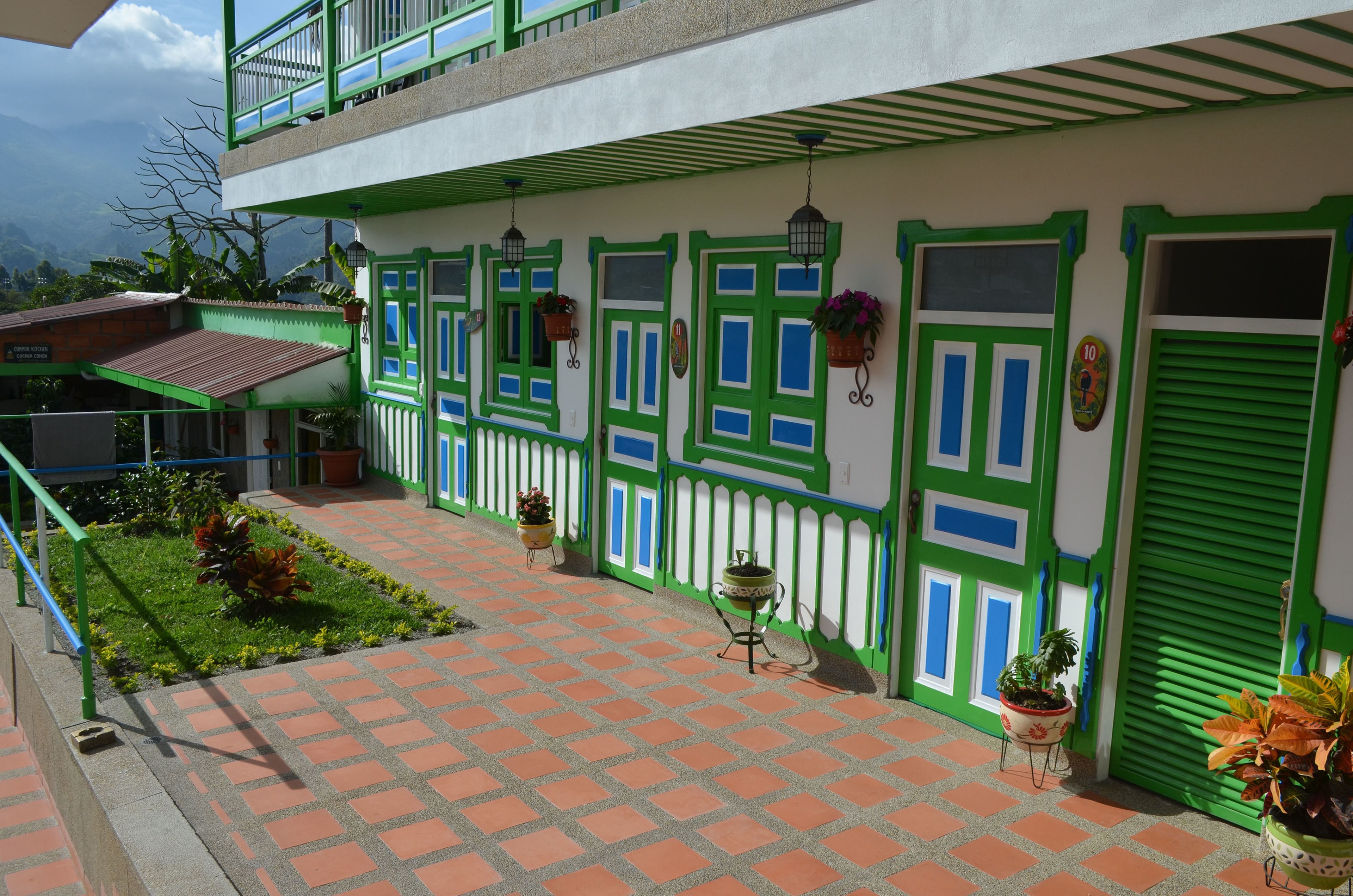 A two-story building with green and white exterior walls, multiple windows with green shutters, and potted plants on the ground floor.