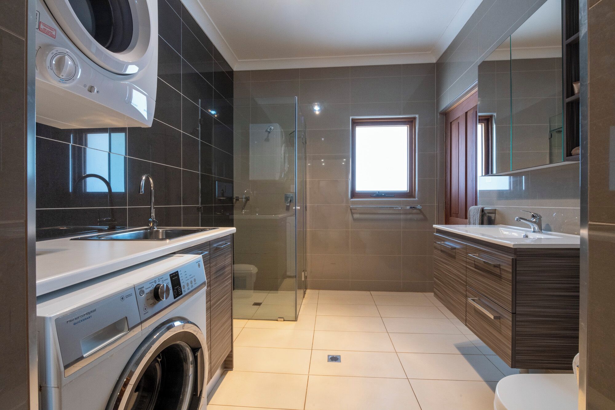 Een moderne badkamer met een wasmachine, een glazen douchecabine en een grote spiegel.