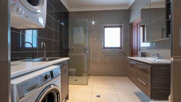 Een moderne badkamer met een wasmachine, een glazen douchecabine en een grote spiegel.