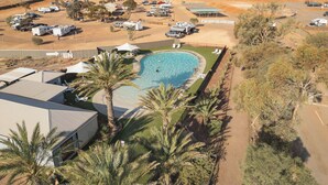 A large swimming pool surrounded by palm trees and a parking area with RVs. - Stuart Range Outback Resort (Coober Pedy)