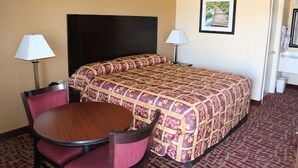 Una habitación de hotel con una cama, dos lámparas de noche, una mesa redonda con sillas y un cuadro en la pared.