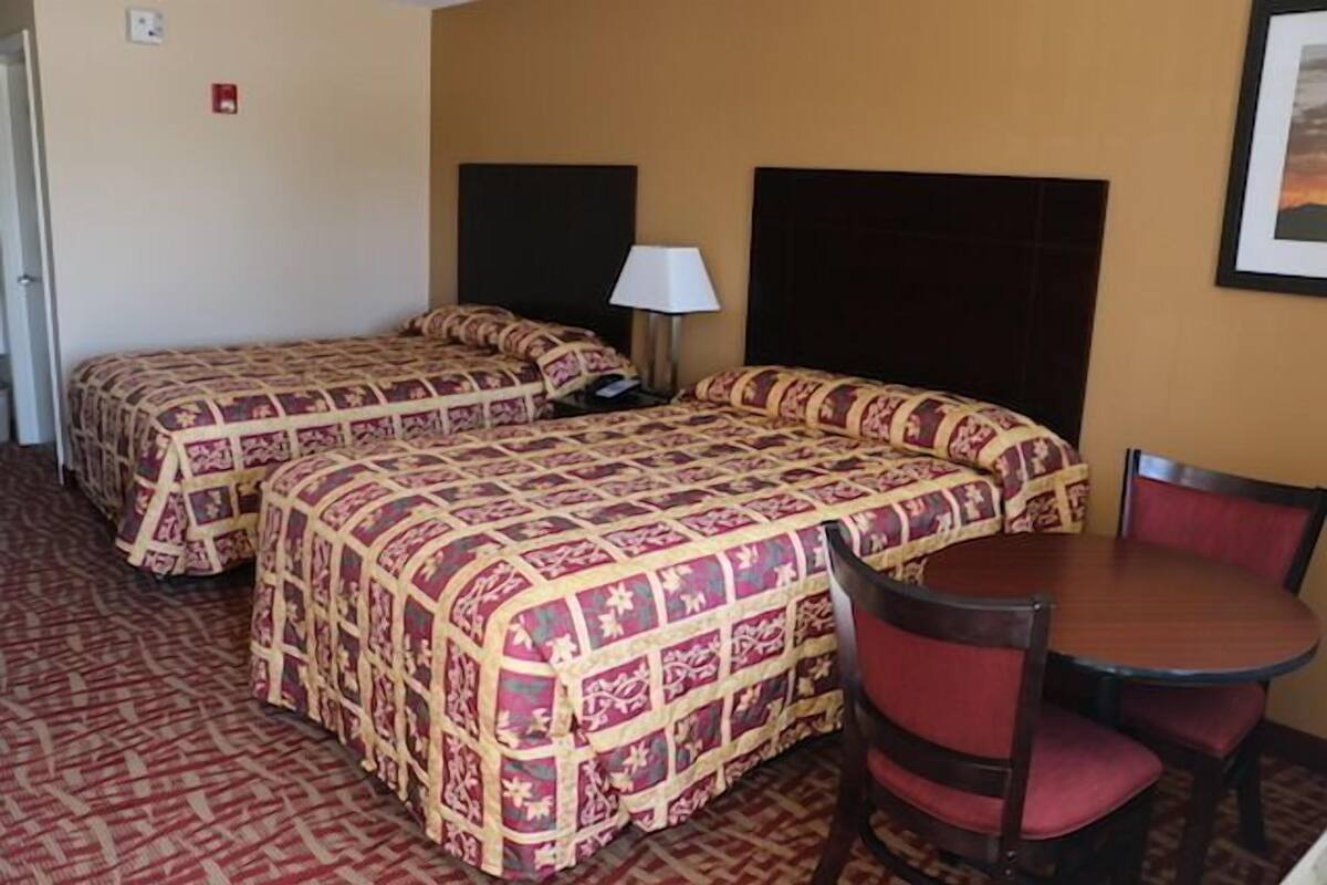 A hotel room with two beds, a table, and chairs.