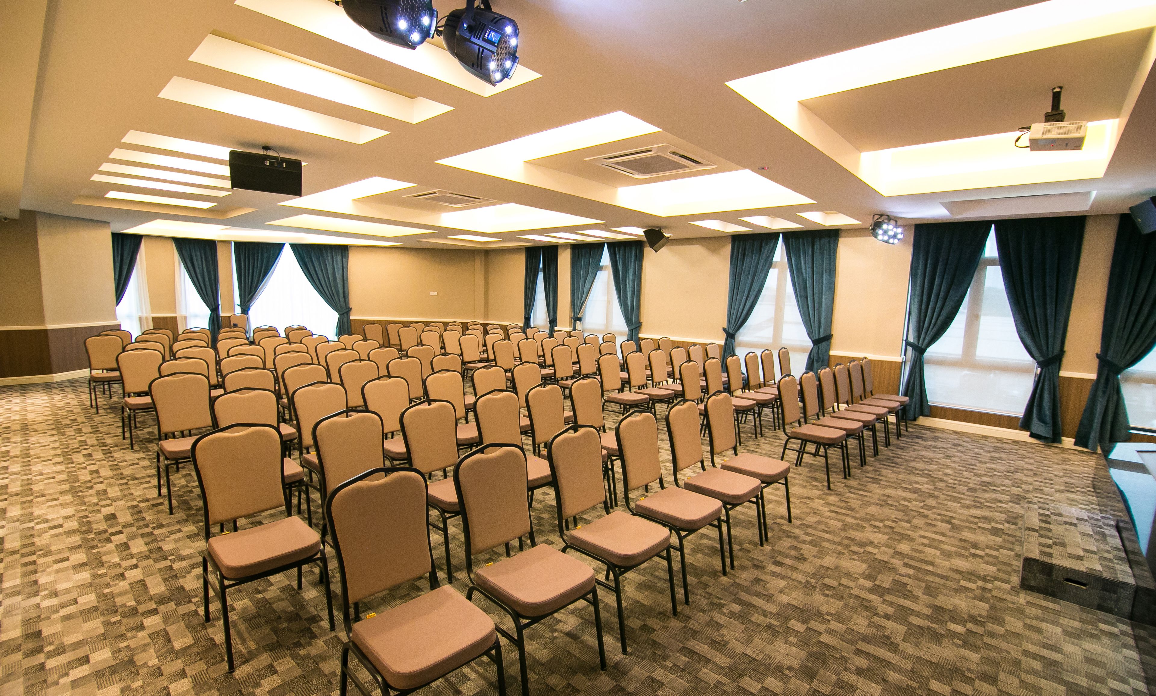 A conference room with rows of chairs, ceiling-mounted projectors, and large windows with curtains.