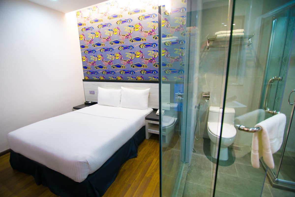 Une chambre d’hôtel avec un lit, une salle de bain dotée d’une douche à parois de verre et un mur orné d’un motif coloré.