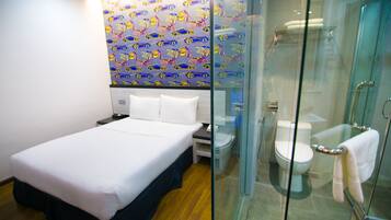 A hotel room with a bed, a bathroom with a glass shower enclosure, and a wall with a colorful pattern.