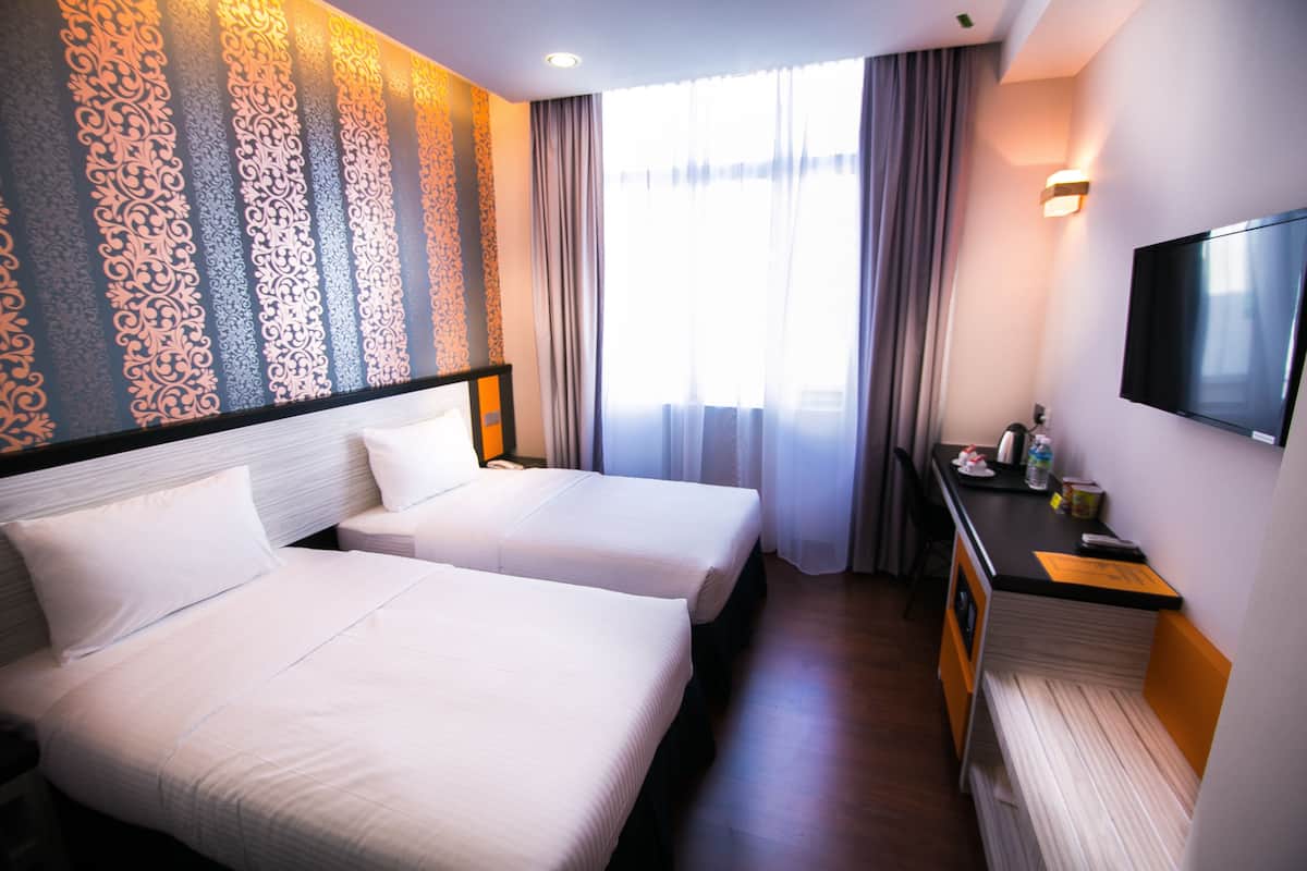 Une chambre d’hôtel avec deux lits, un bureau doté d’un téléviseur à écran plat et une grande fenêtre avec des rideaux.