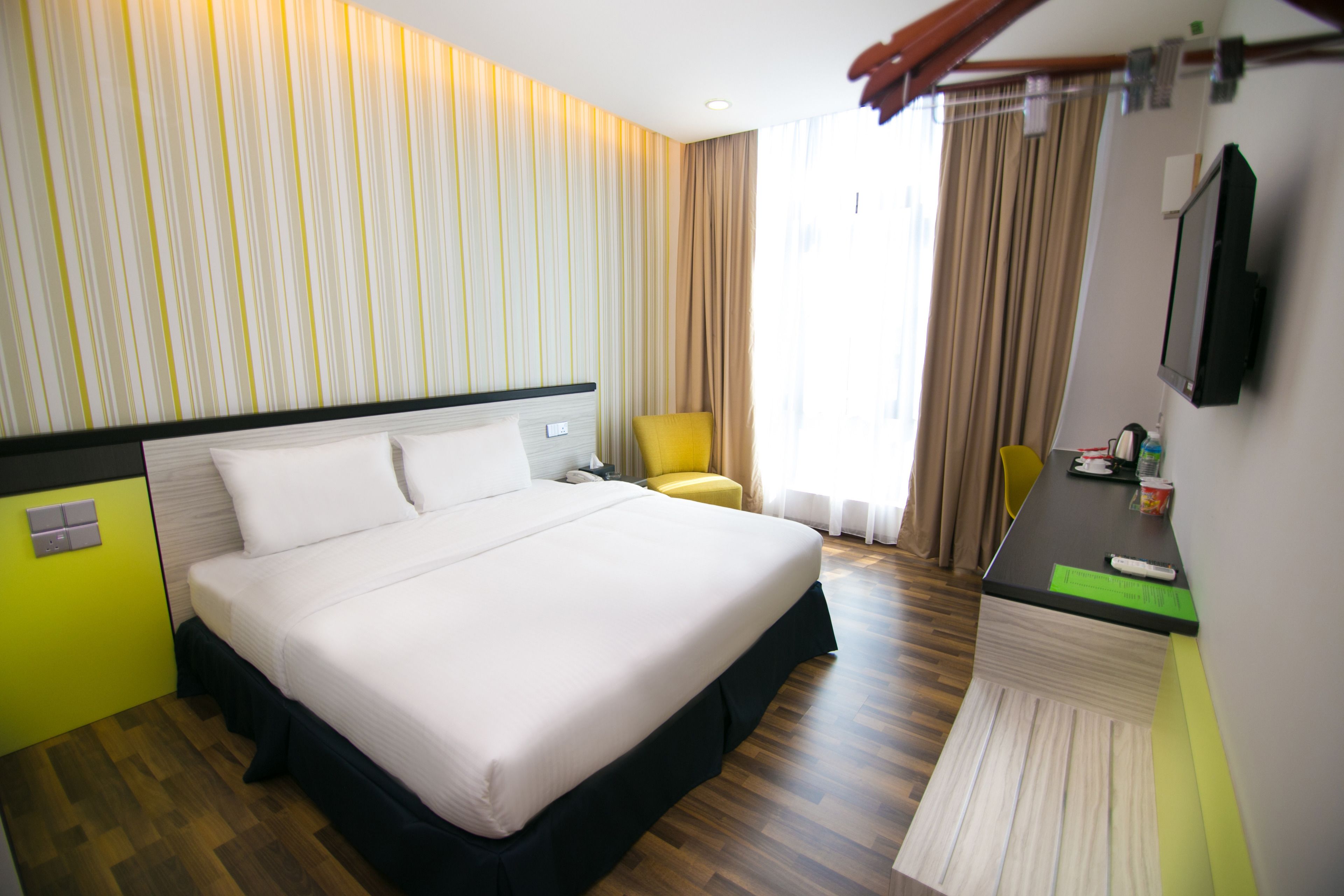 A hotel room with a large bed, a desk with a chair, a television, and a window with curtains.