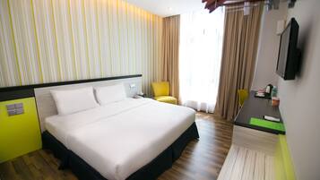 A hotel room with a large bed, a desk with a chair, a television, and a window with curtains.