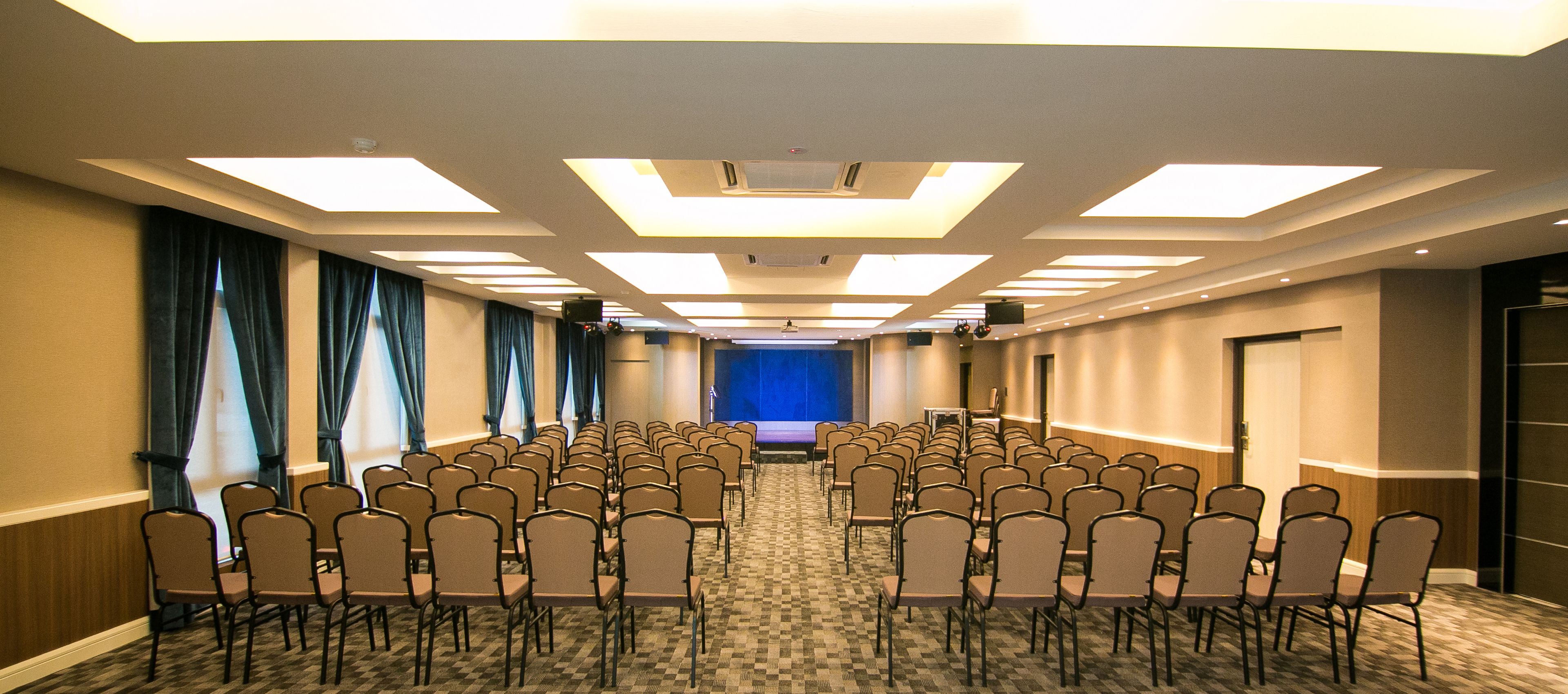 A conference room with rows of chairs, a stage, and a blue screen at the front.