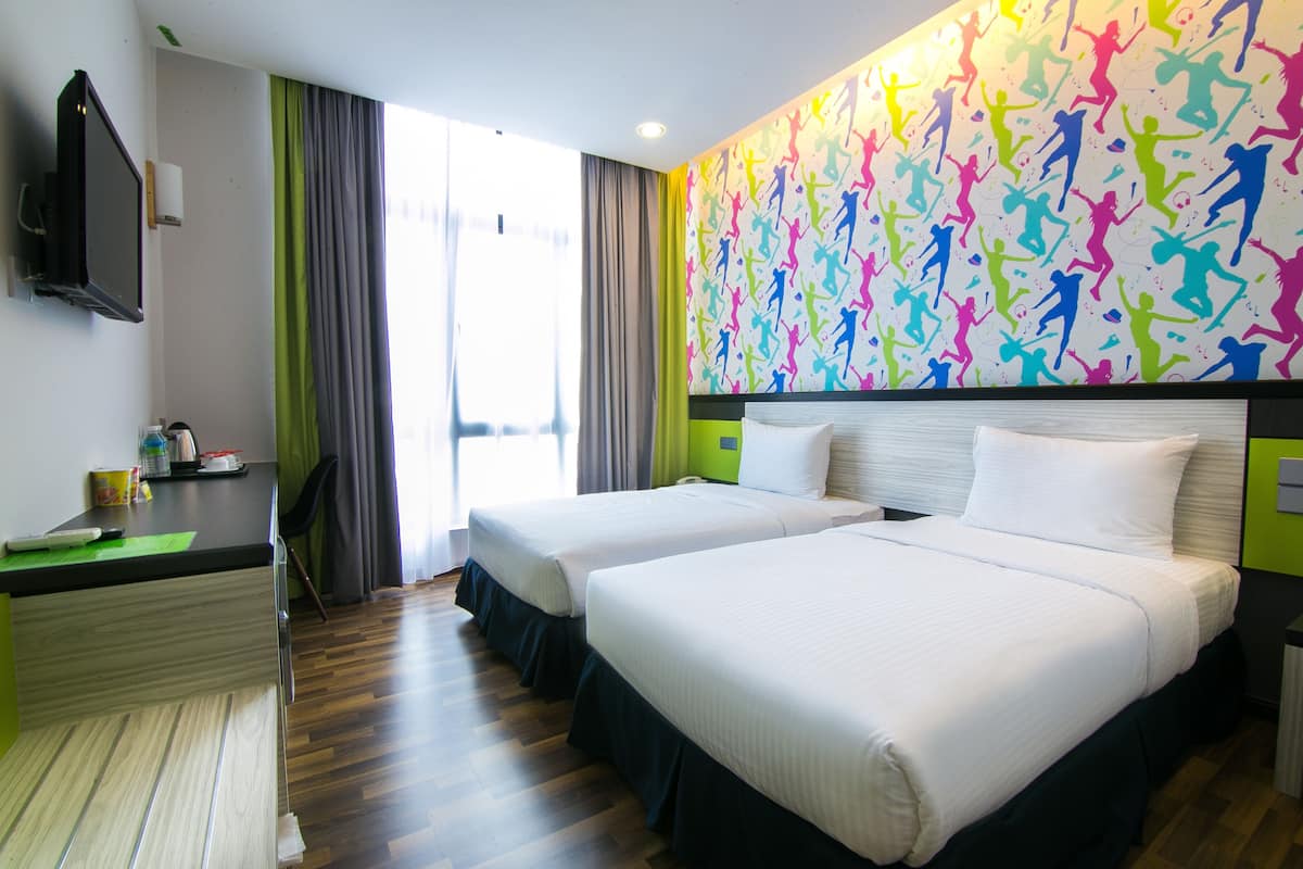 Une chambre d’hôtel avec deux lits, un bureau, une télévision et une fresque murale aux couleurs vives.