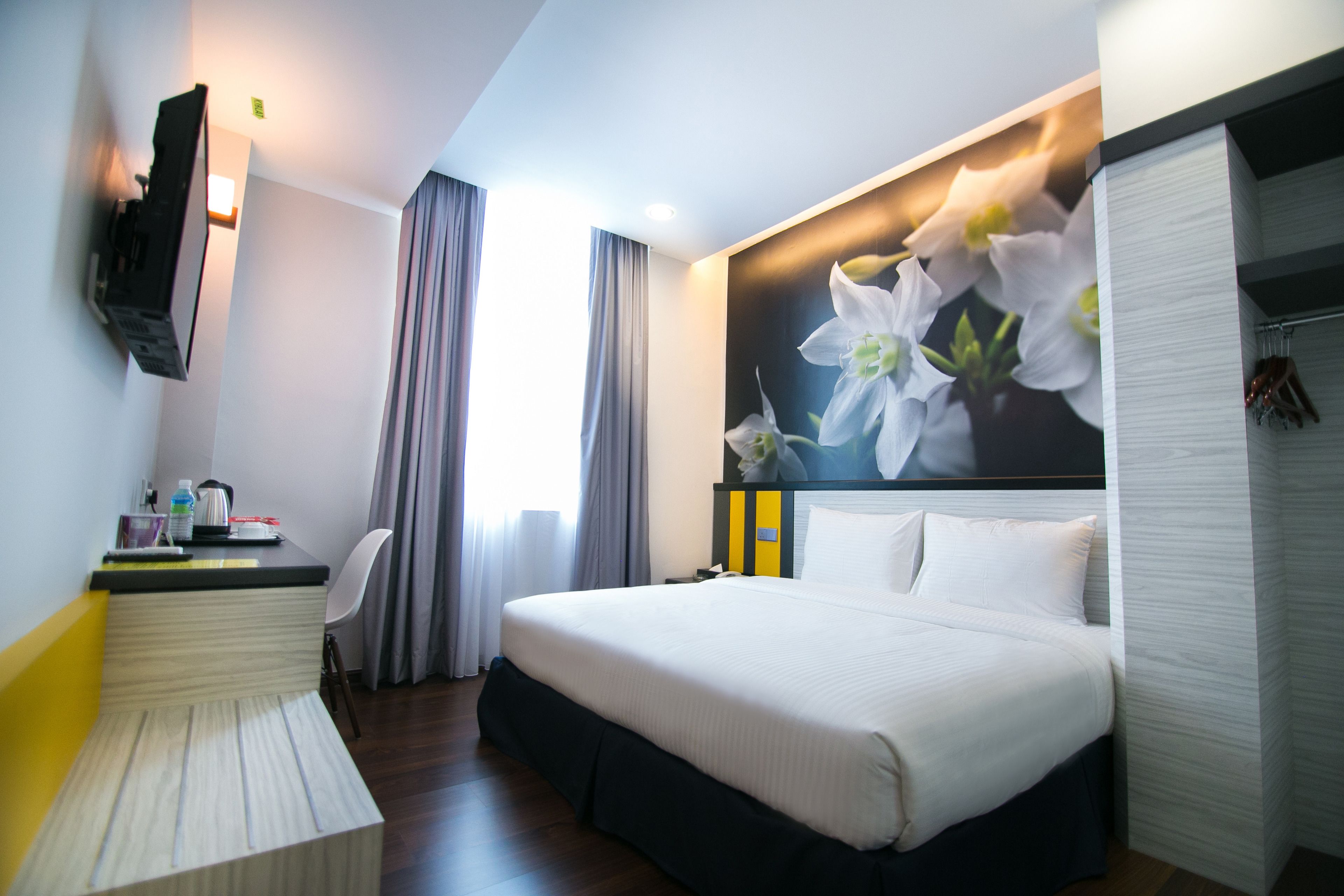 Una habitació d'hotel amb un llit, un escriptori, una cadira i una televisió penjada a la paret.