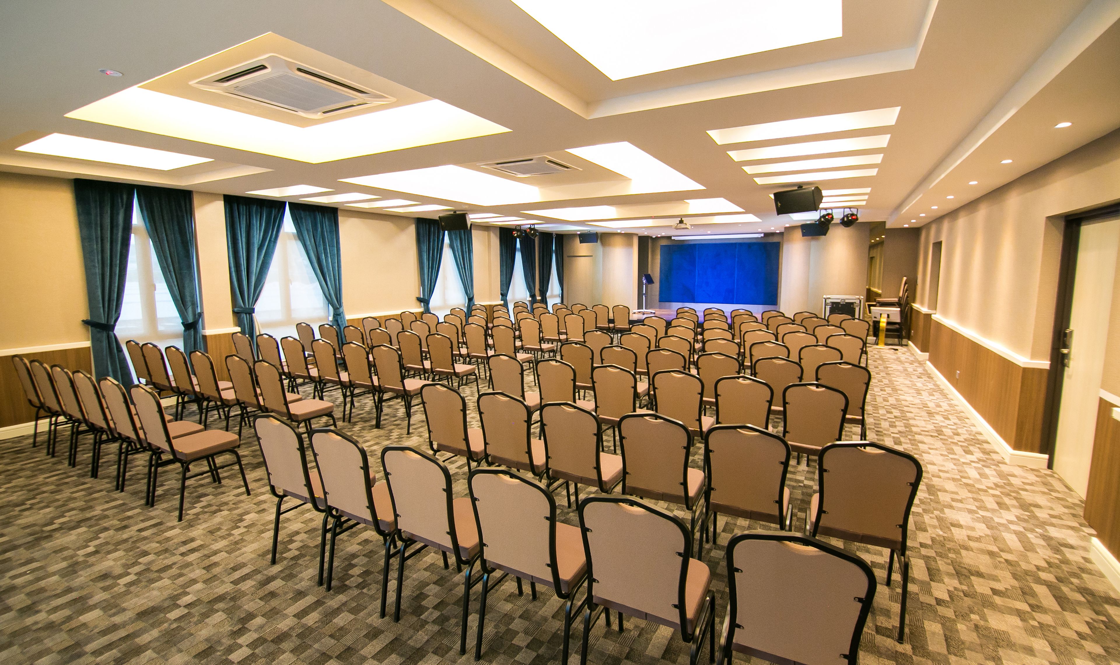 Una sala conferenze con file di sedie e tavoli, un palco con uno sfondo blu e un proiettore.