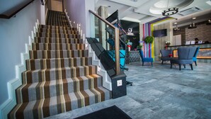 Un moderno vestíbulo de hotel con una escalera, una recepción y una zona de estar.