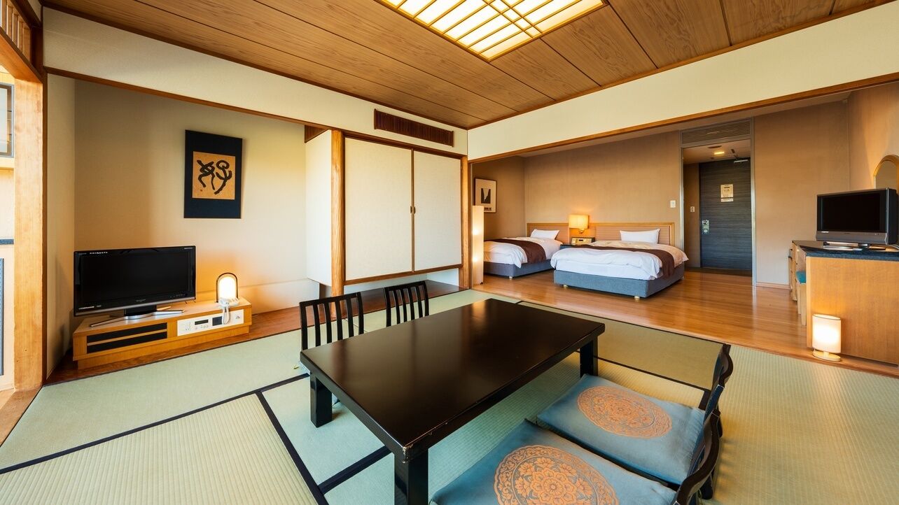 A traditional Japanese-style room with tatami flooring, a low table, a television, and a bed with a wooden headboard.