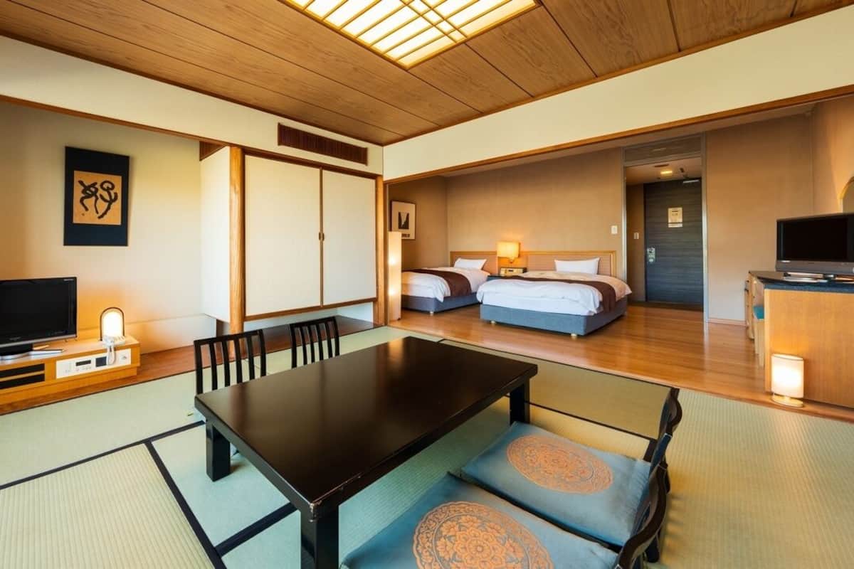 A traditional Japanese-style room with tatami flooring, a low table, a television, and a bed with a wooden headboard.