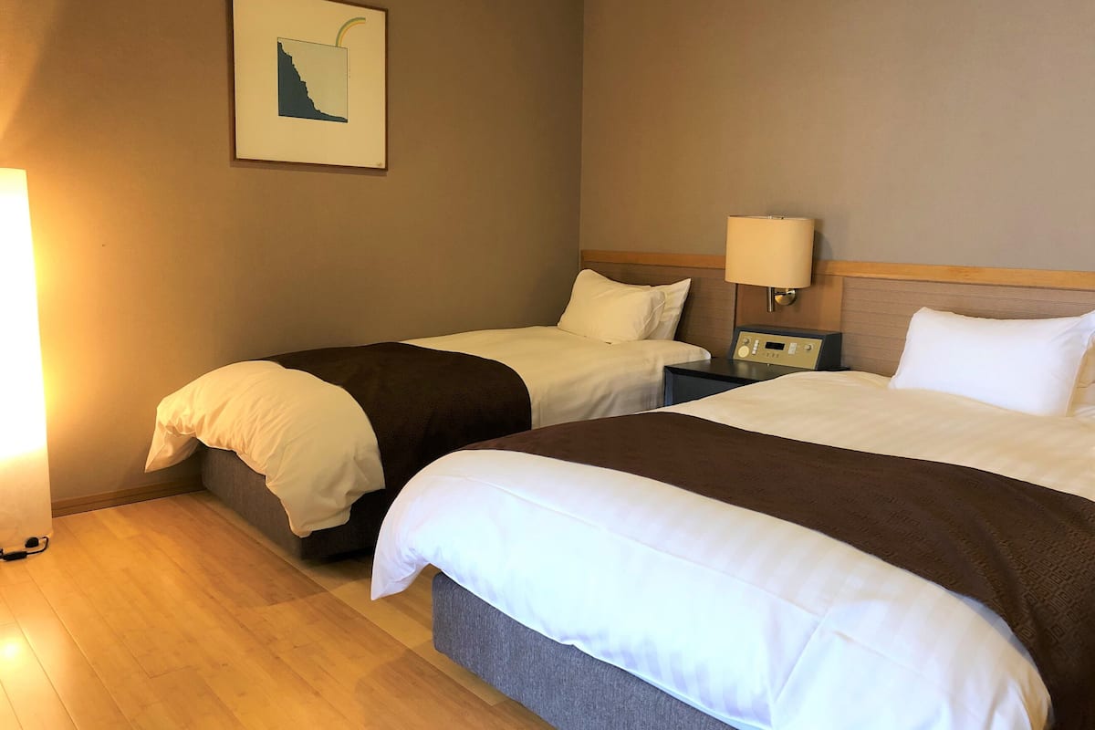 A hotel room with two beds, a nightstand, a lamp, and a framed picture on the wall.