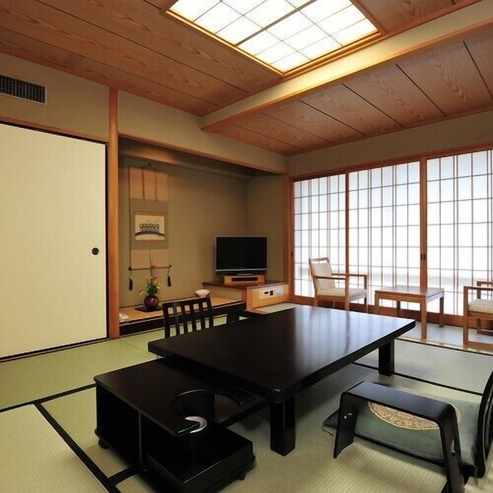Una habitación tradicional japonesa con suelo de tatami, una mesa baja, un televisor y puertas correderas.