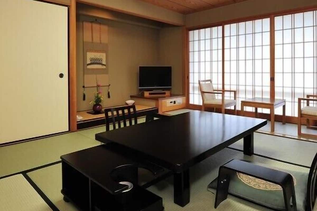 A traditional Japanese room with tatami flooring, a low table, a television, and sliding doors.