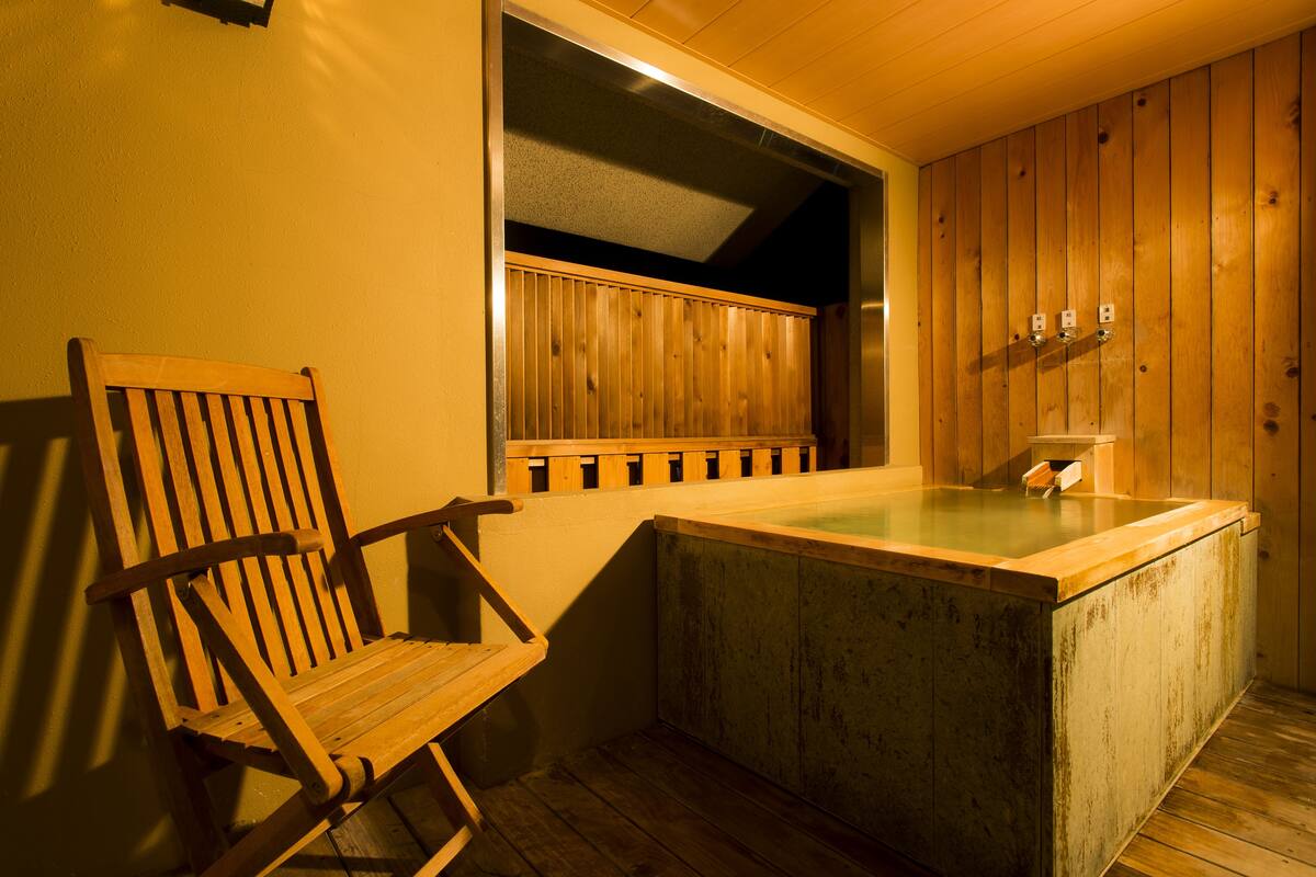 A wooden sauna with a bench, a glass-enclosed hot tub, and wooden paneling on the walls.