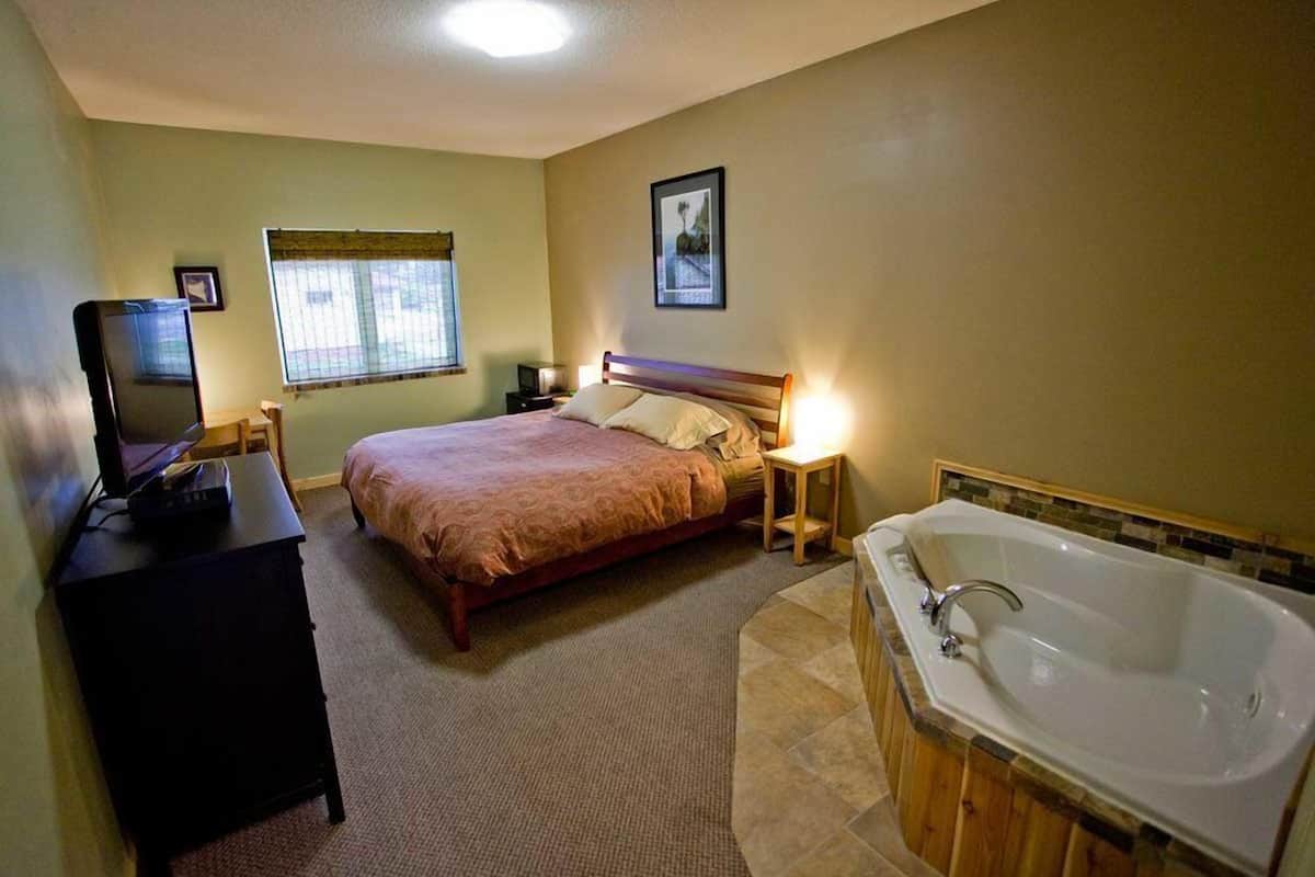 Ein Schlafzimmer mit Bett, Nachttisch, Lampe, Fernseher und einer großen Badewanne.