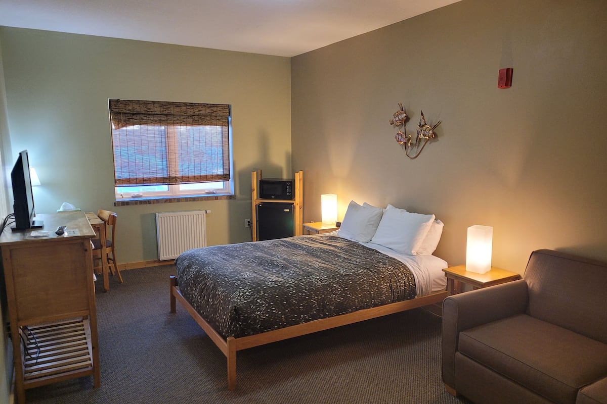 Ein Hotelzimmer mit Bett, Schreibtisch, Stuhl, Mikrowelle und Lampe.